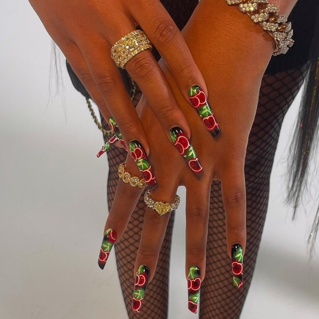 unhas-cereja-megan-thee-stallion Foto das mãos da rapper Megan Thee Stallion com destaque para as unhas longas com decoração de desenho de cereja.