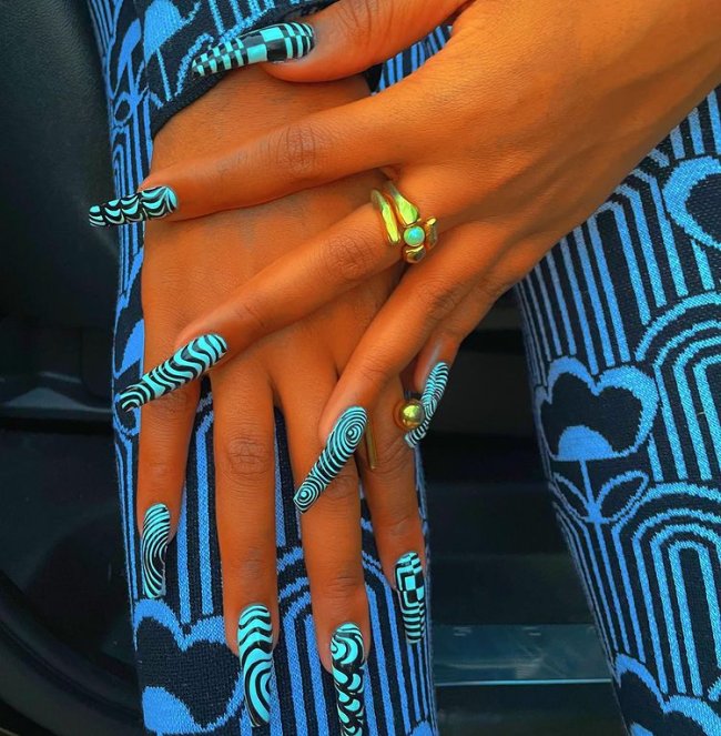 unhas-psicodelicas-megan-thee-stallion Foto das mãos da rapper Megan Thee Stallion com destaque para as unhas longas com decoração preta e branca em uma estampa psicodélica.