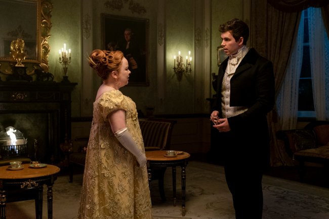 BRIDGERTON_208_Unit_02602R Nicola Coughlan como Penelope Featherington e Luke Newton como Colin Bridgerton conversando em uma sala de frente um para o outro