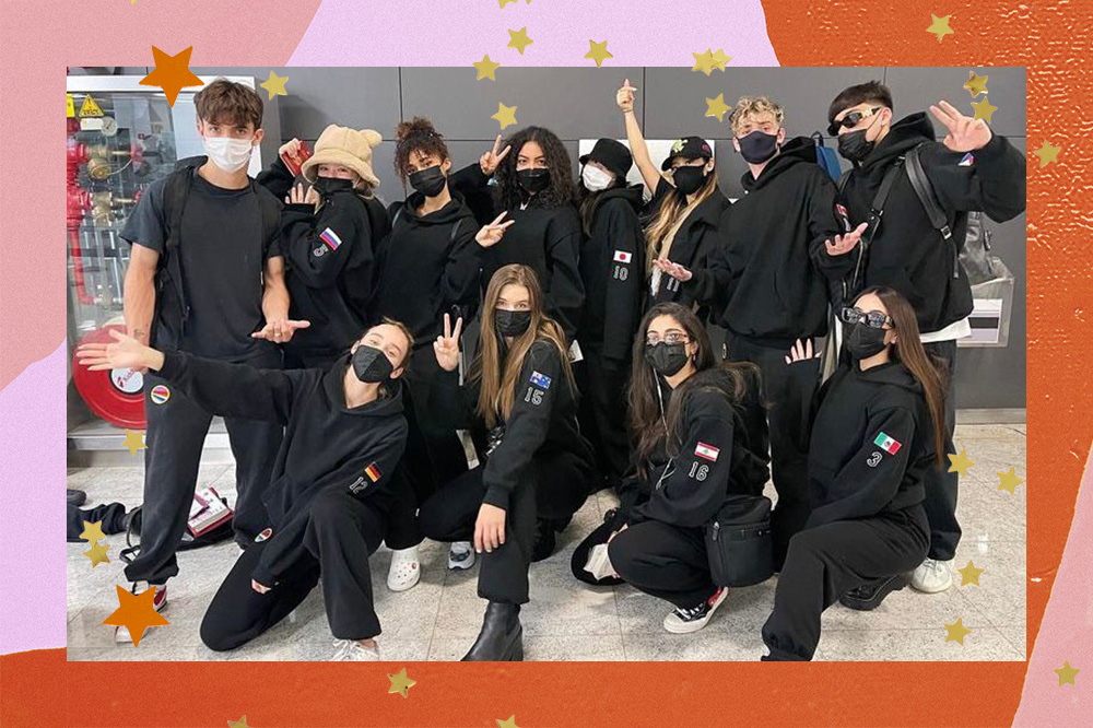Imagem mostra integrantes do Now United reunidos em sua chegada ao Brasil. O grupo veste um uniforme de moletom preto com numeração e as respectivas bandeiras dos países. A montagem segue acompanhada de uma borda colorida e estrelinhas douradas por toda a imagem.