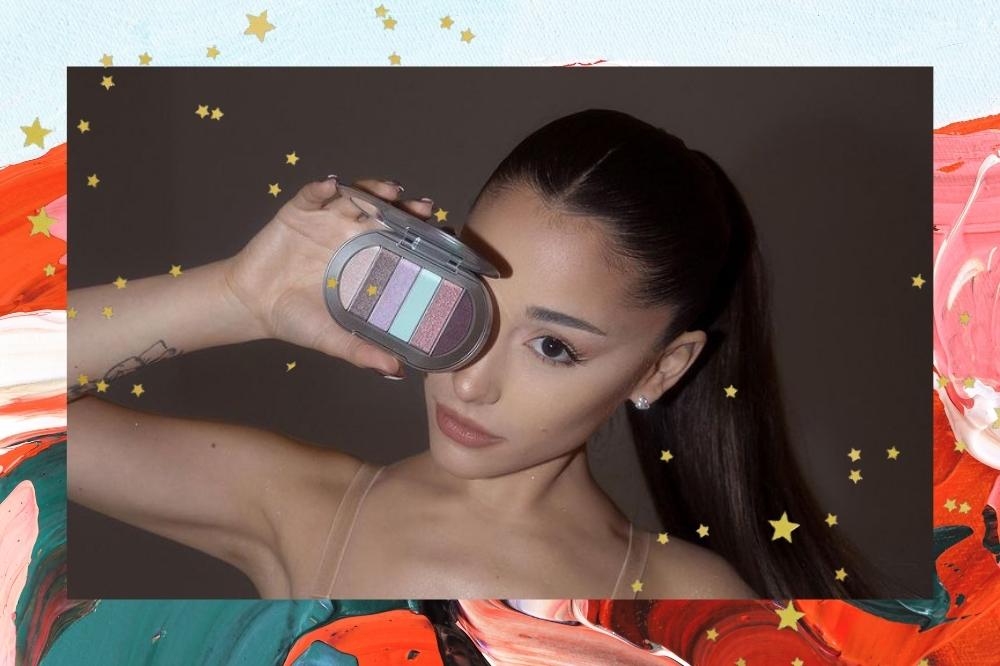 Montagem com o fundo colorido e detalhe de estrelinhas douradas na borda com a foto da Ariana Grande no centro. Na foto ela está com uma maquiagem básica, cabelo preso em um rabo de cavalo, segura uma paleta de sombras com a mão direita e a coloca sob o olho direito. Ela olha para a câmera e não sorri.