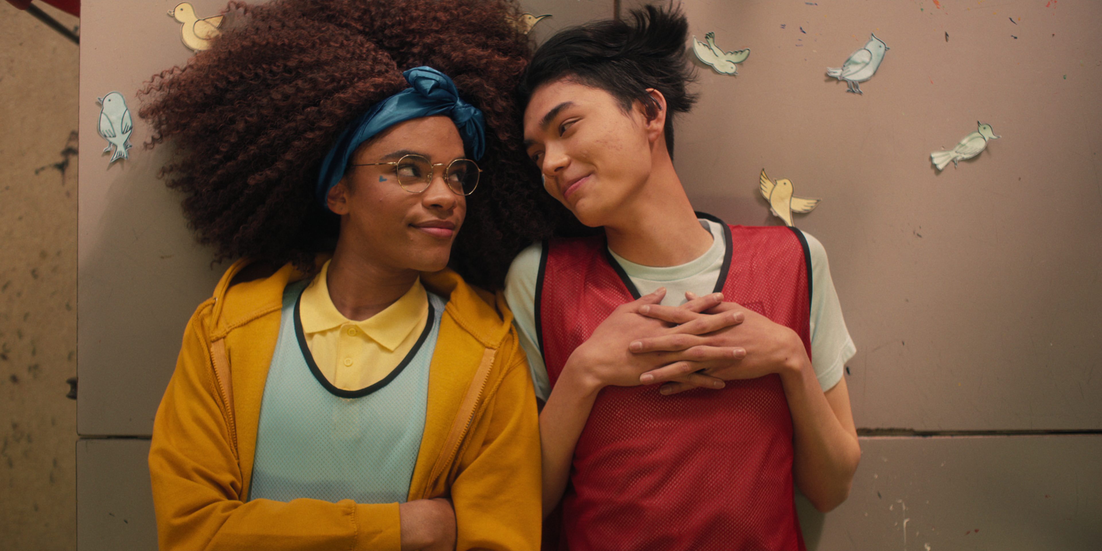 heartstopper-netflix-elle-tao Elle Argent (Yasmin Finney) e Tao Xu (William Gao) em Heartstopper. Eles estão deitados em cima de uma mesa da escola, olhando um para o outro.