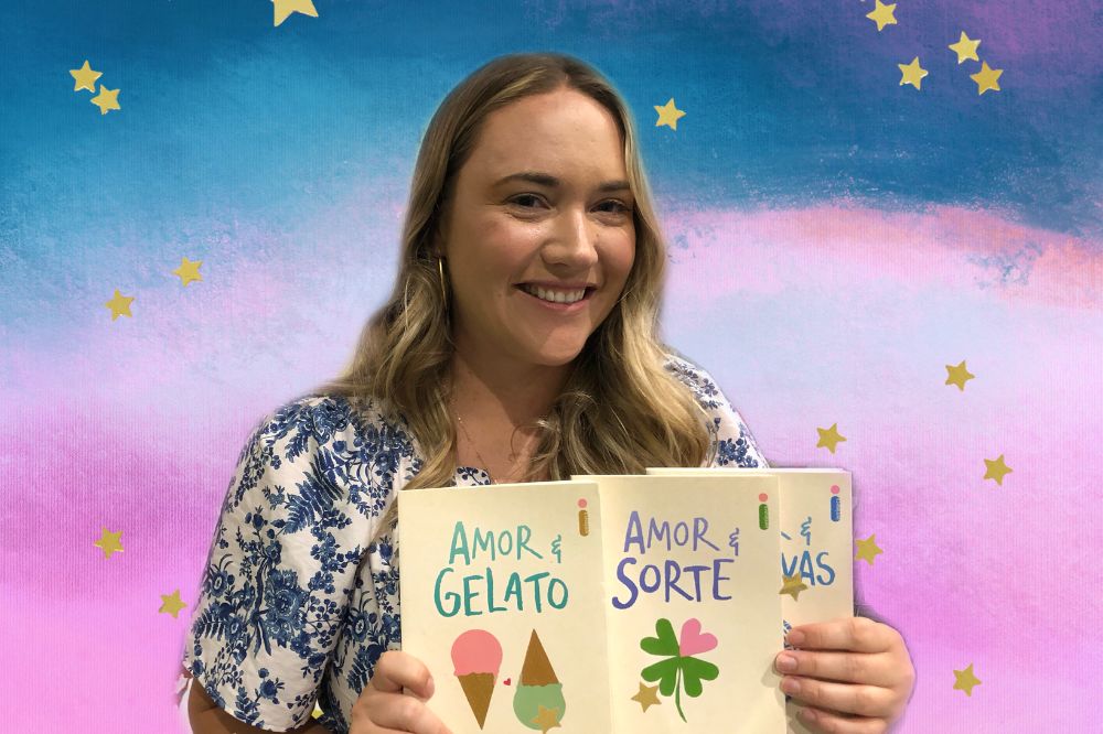 Jenna Evans Welch sorrindo para foto e segurando livros da coleção Amor &; o fundo é uma textura nas cores azul, branco, roxo e rosa com estrelas amarelas decorando a imagem