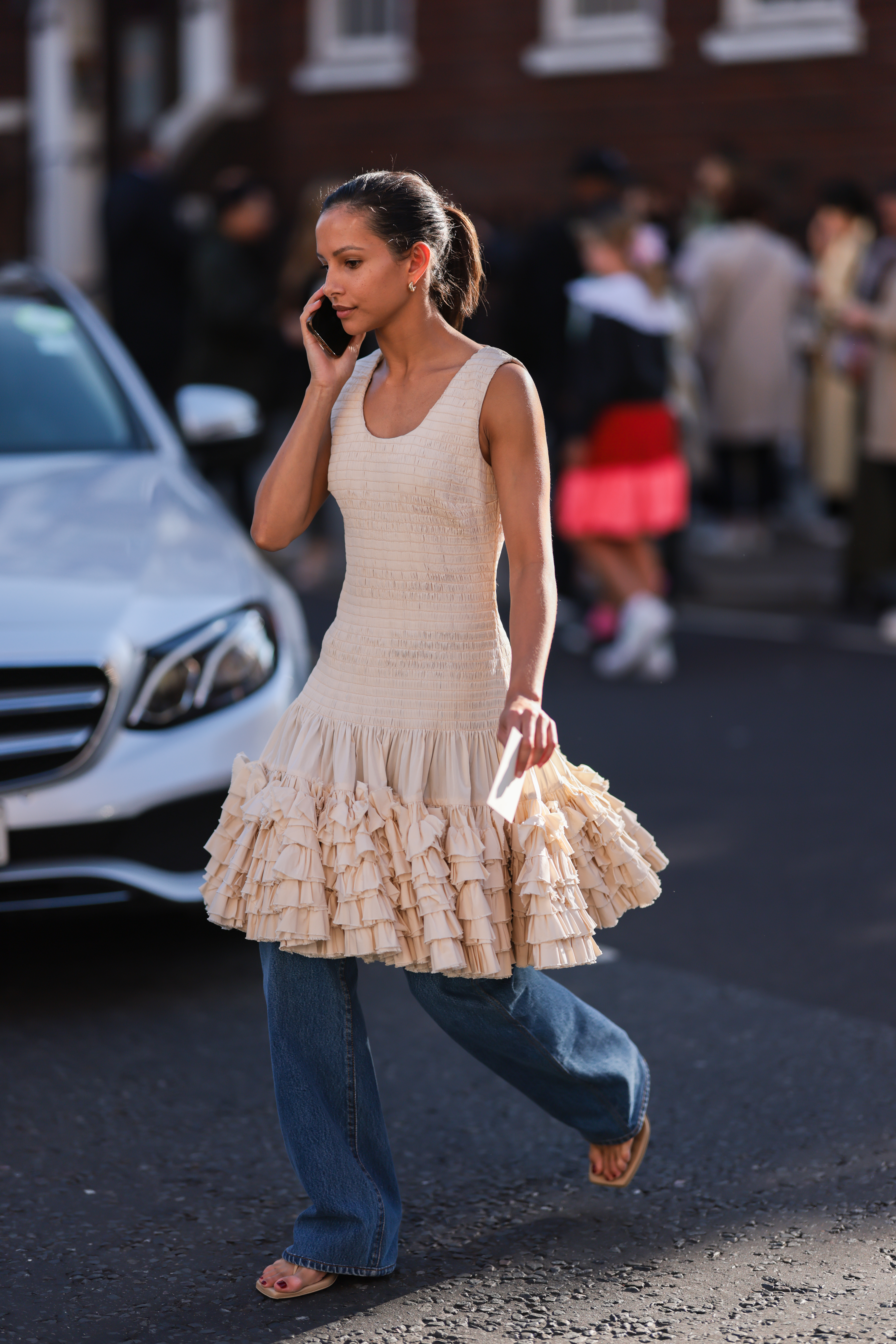 Mulher usando vestido rosa claro de babados por cima de calça jeans enquanto anda na rua na semana de moda de Londres