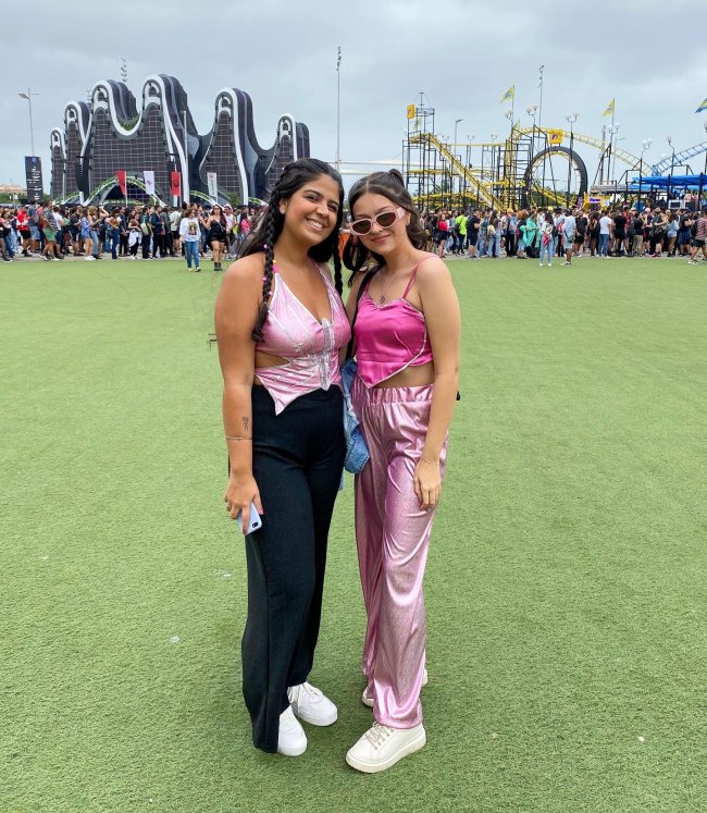 looks-rosa-rock-in-rio-2022 Foto de duas meninas no Rock in Rio 2022. Ambas usam looks com peças rosas, olham para a câmera e sorriem.