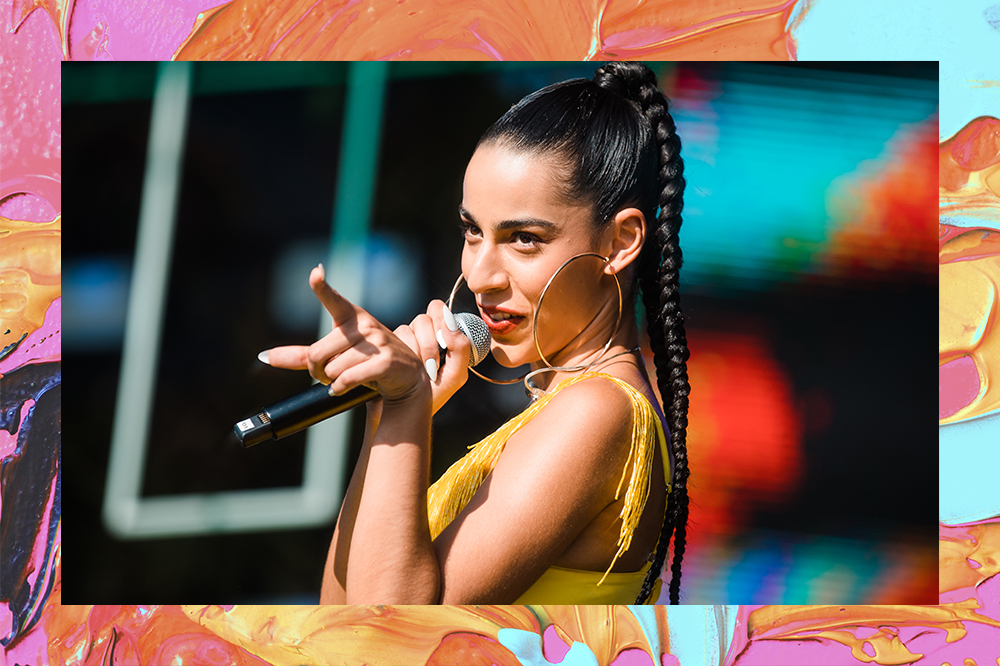 Montagem em fundo laranja, rosa, azul e amarelo de foto de Marina Sena cantando em palco e apontando dedo para platéia