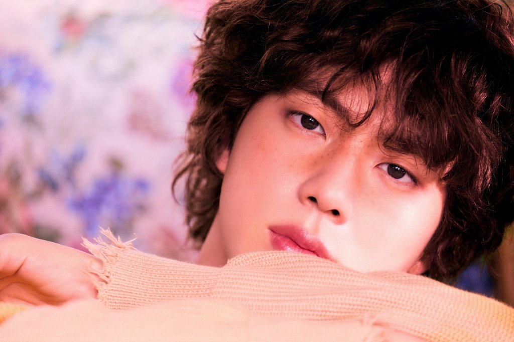 Jin posando para foto com expressão neutra enquanto olha para câmera