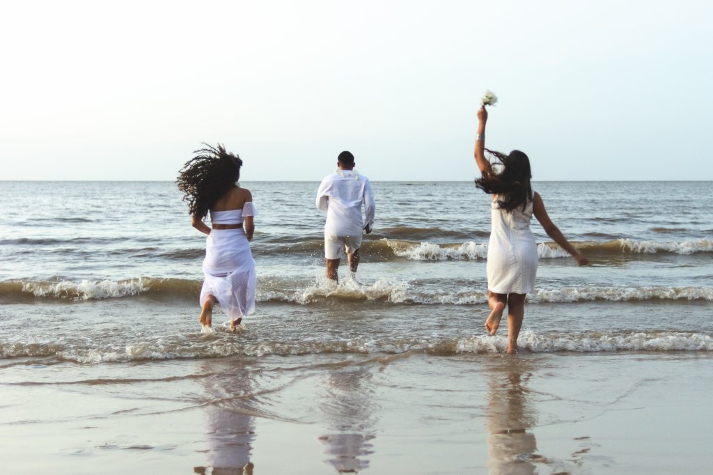 Amigos felizes comemorando o réveillon na praia, correndo para o mar e pulando ondas. Eles usam roupas brancas. Grupo de jovens curtindo e festejando juntos. Conceitos de felicidade, união, juventude e véspera de ano novo.