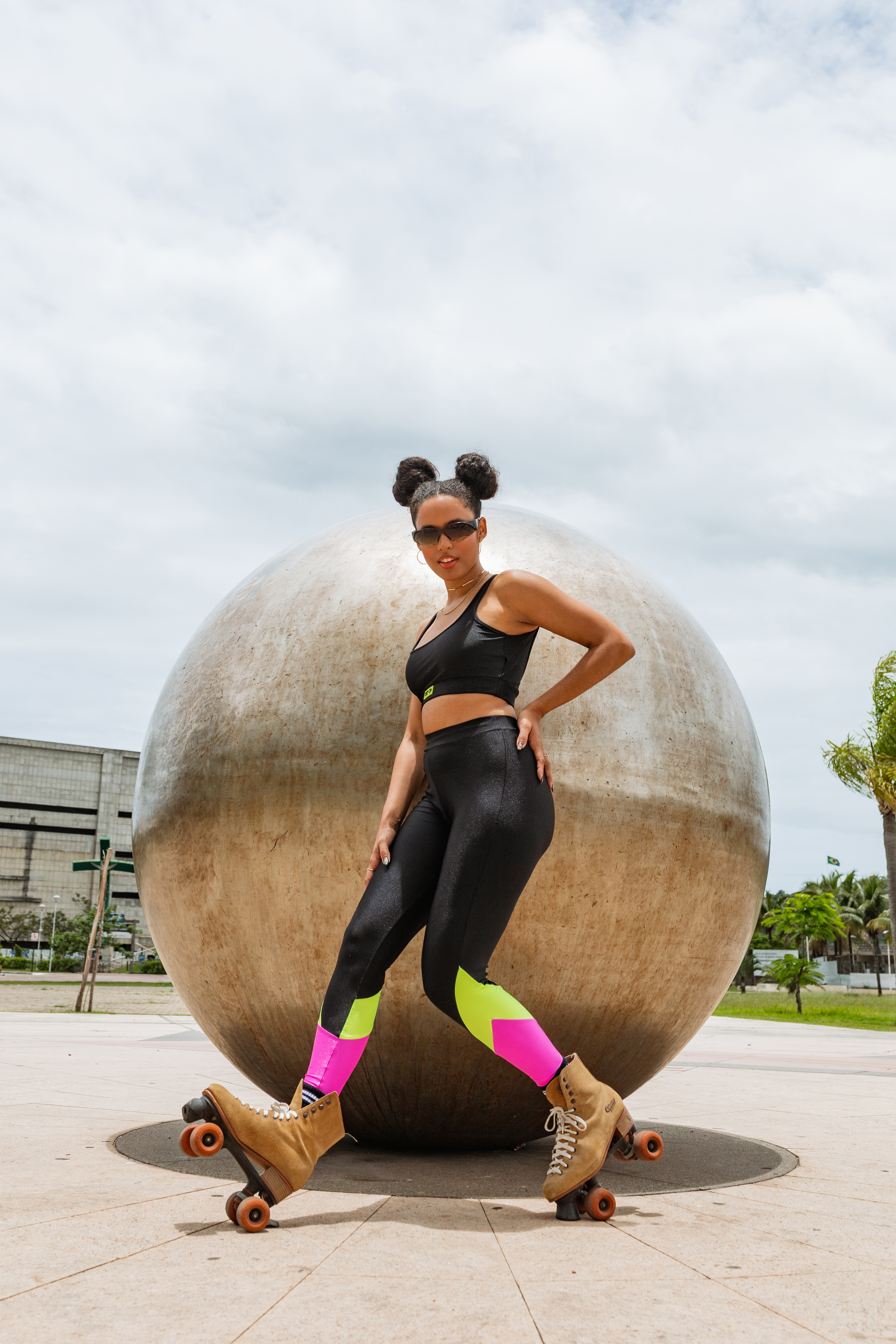 Modelo usando top e legging preta com rosa e verde neon da Coleção de roupas da CAPRICHO com a Agua Azul no mood Aguete Joy enquanto anda de patins