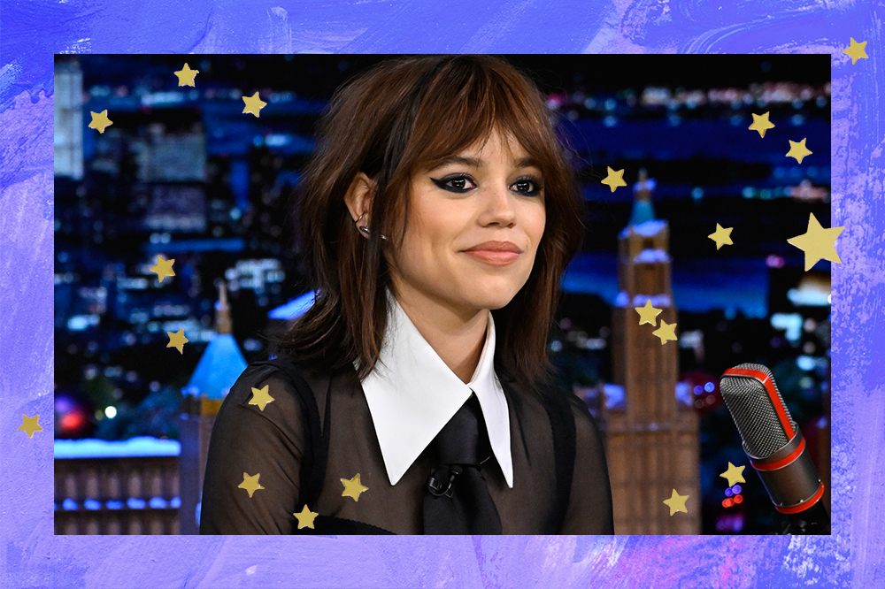 Jenna Ortega em entrevista no Jimmy Fallon sorrindo sem mostrar os dentes. Montagem com fundo azul e estrelinhas douradas