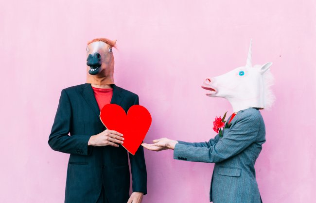 Casamento às Cegas prova que aparências importam bem mais do que deveriam Duas pessoas vestidas de terno e com máscaras de cavelo. Uma delas entrega um coração vermelho para outra