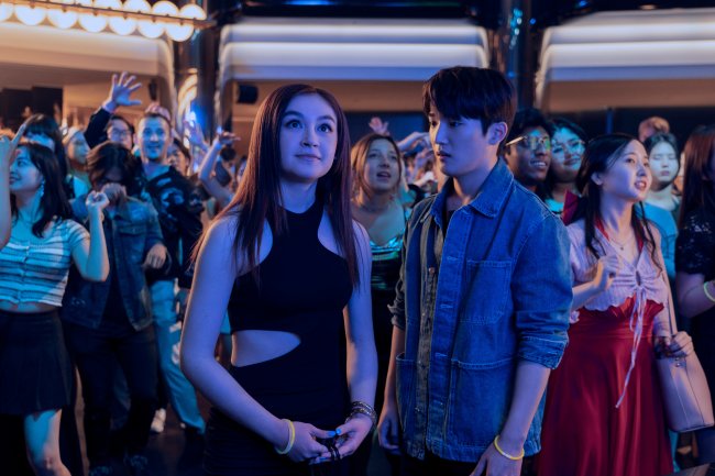 XO_106_Unit_00515RC Anna Cathcart como Kitty Song Covey e Choi Min-yeong como Dae em XO, Kitty; eles estão em uma festa iluminados por luzes na cor azul e rodeados por outras pessoas