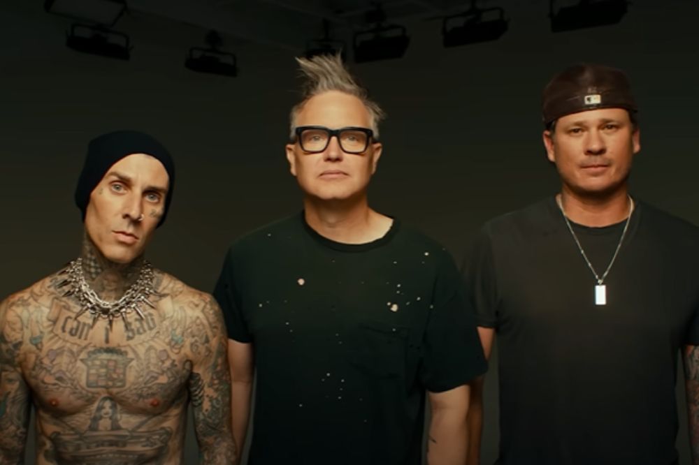 Integrantes do blink-182 reunidos posando na frente de um fundo preto com expressões neutras