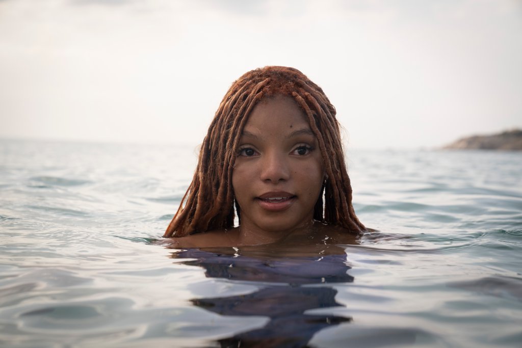 Halle Bailey como Ariel no live-action de A Pequena Sereia, da Disney; ela está mo mar, dentro da água, sorrindo levemente