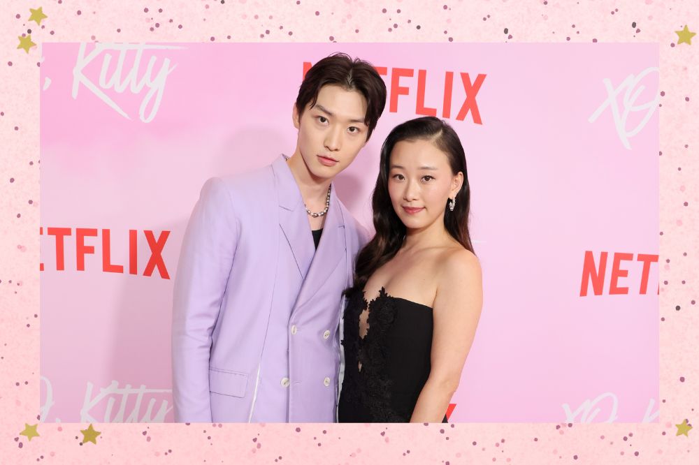 Sang Heon Lee e Gia Kim, de Com Carinho, Kitty na première da série em Los Angeles; eles estão abraçados posando para foto; a margem é uma textura nas cores rosa com bolinhas