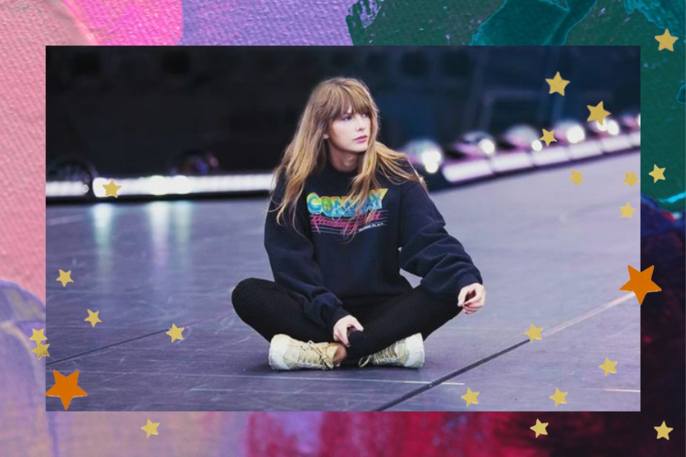 Montagem com fundo rosa, lilás e verde. Taylor Swift no ensaio da turnê The Eras Tour. Ela veste calça legging preta, moletom azul marinho e tênis bege. Seu cabelo está solto e ela segura um microfone.