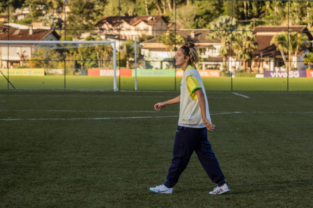 Jogadora no meio do campo usa camiseta da seleção brasileira e calça azul marinho