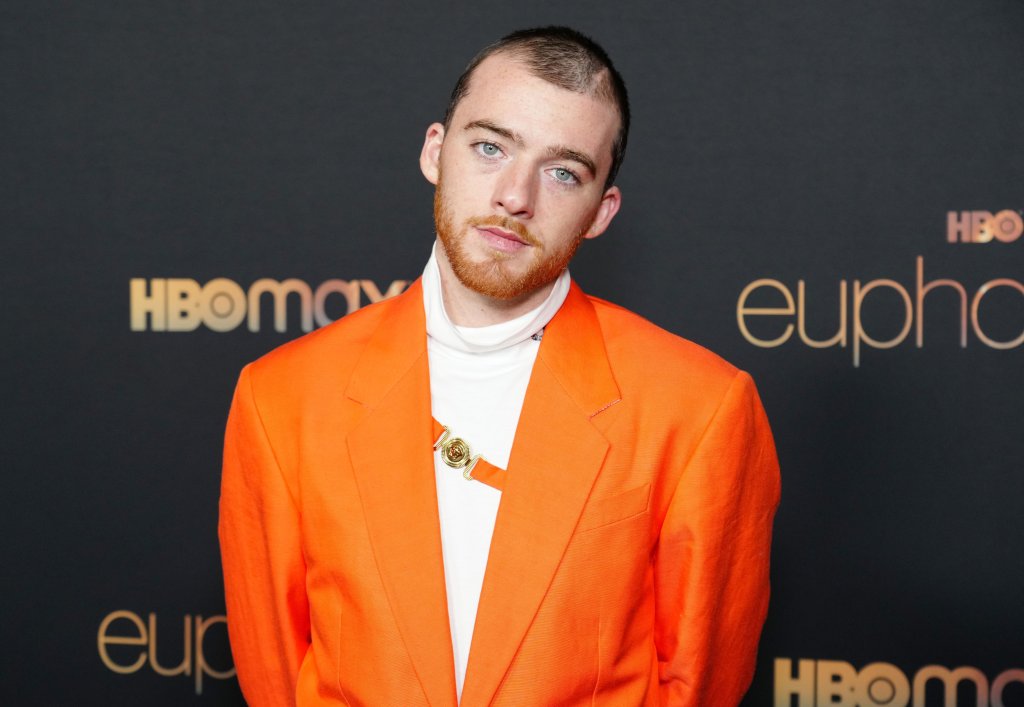 Angus Cloud com os braços para trás e expressão neutra usando roupa laranja e branca em tapete vermelho de evento de Euphoria