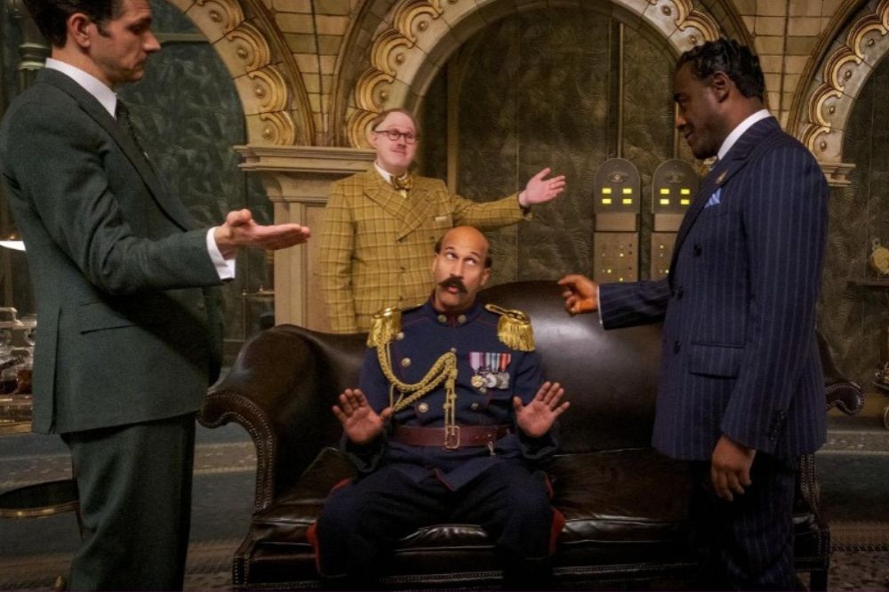 Cenas em Wonka me incomodaram O Chefe de Polícia, interpretado por Keegan-Michael Key, sentado no meio dos três empresários do cartel do chocolate, enquanto é subornado.