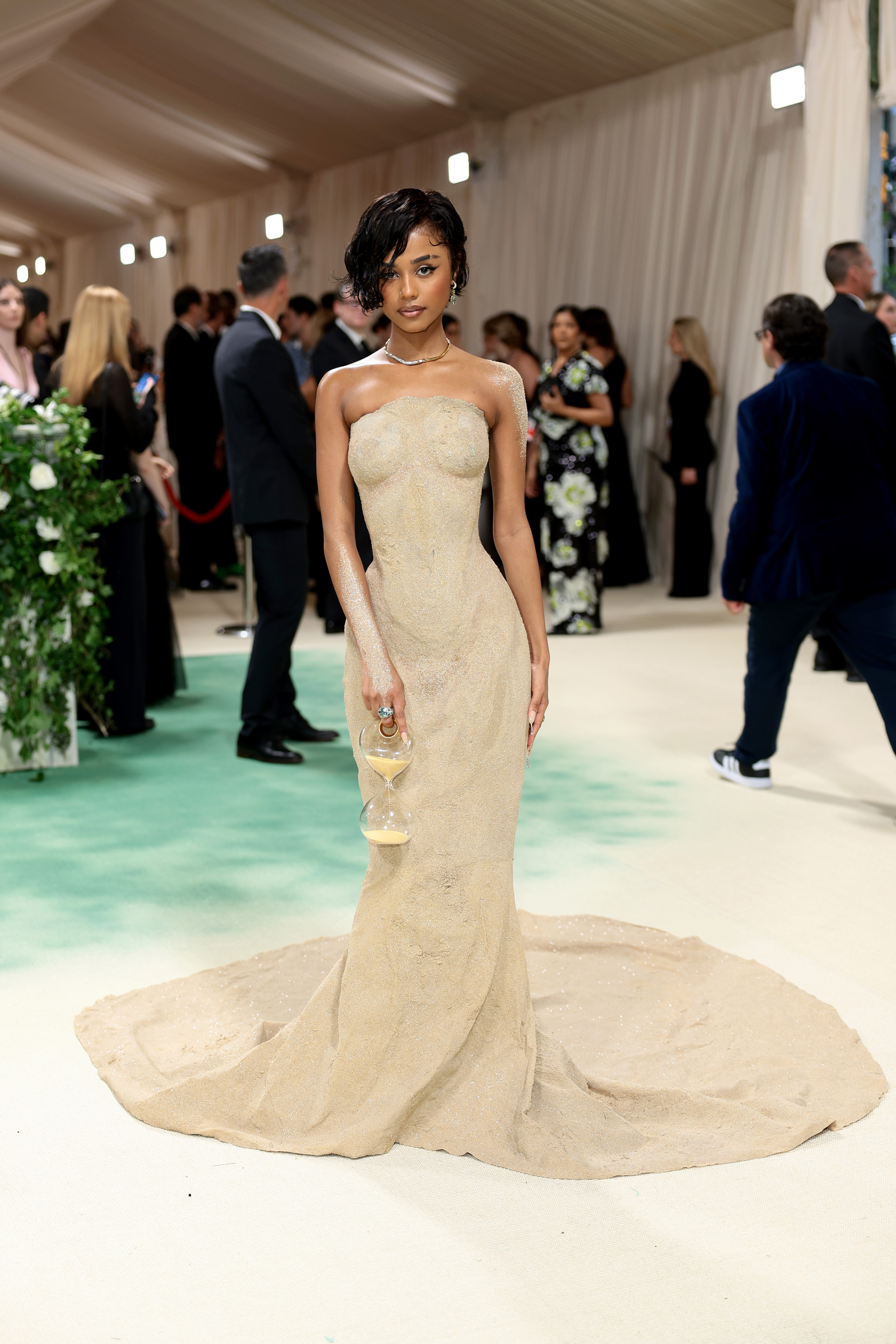 tyla met gala 2024 Tyla posando para foto no MET Gala 2024 com vestido que imita areia; ela segura uma ampulheta e usa areia nos braços