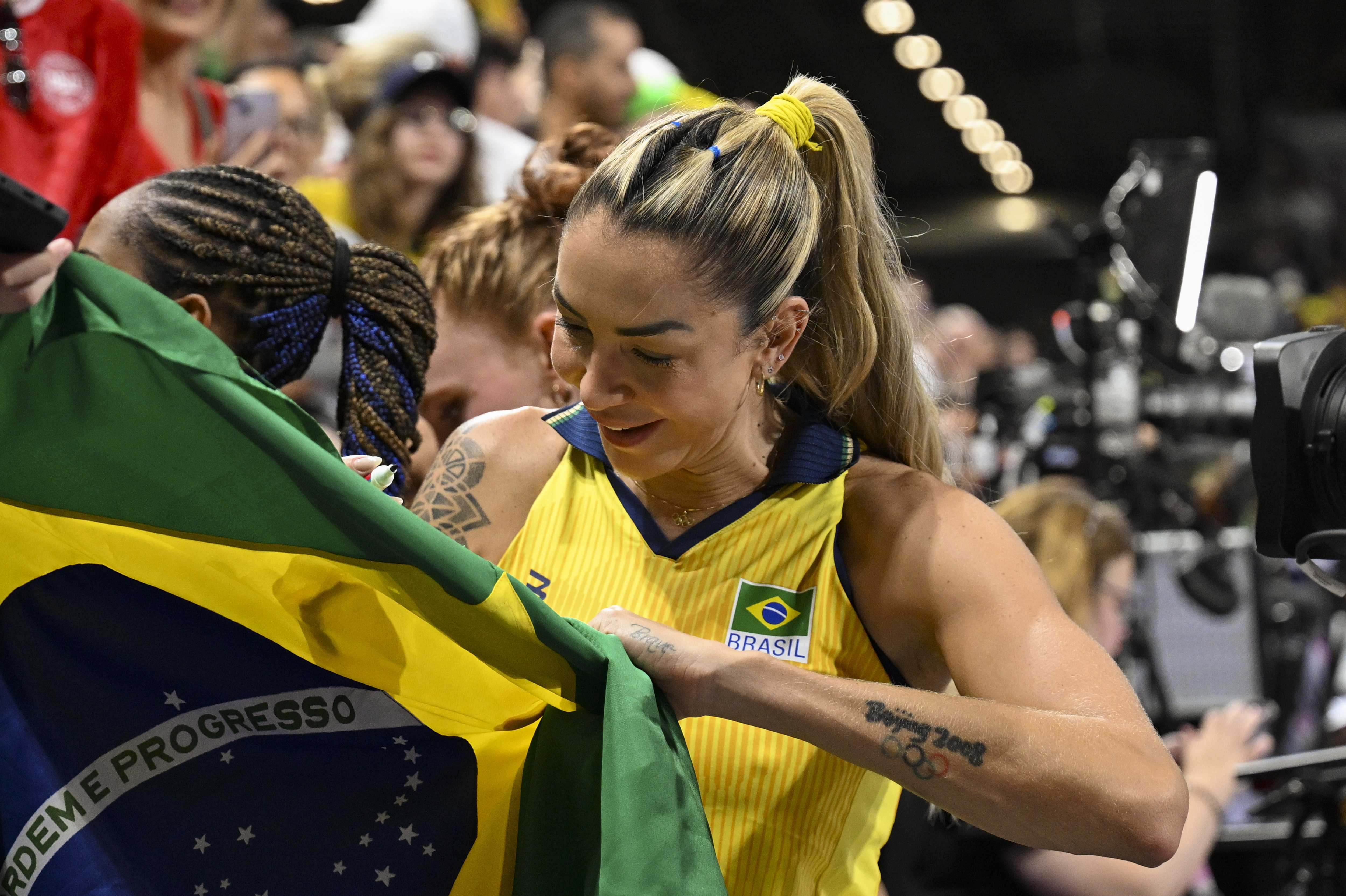 Imagem da jogadora de vôlei Thaisa, vestindo uniforme amarelo e dando autógrado.