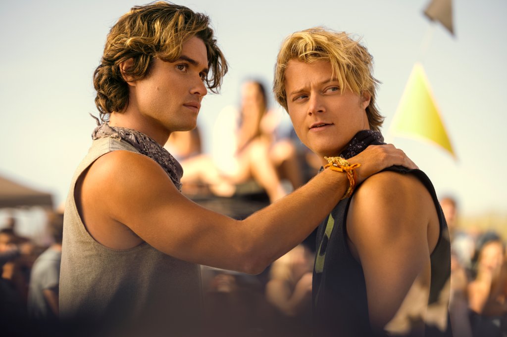Cena de Outer Banks com Chase Stokes como John B e Rudy Pankow como JJ na 4ª temporada; John B está com uma das mãos no ombro de JJ e os dois olham para o lado
