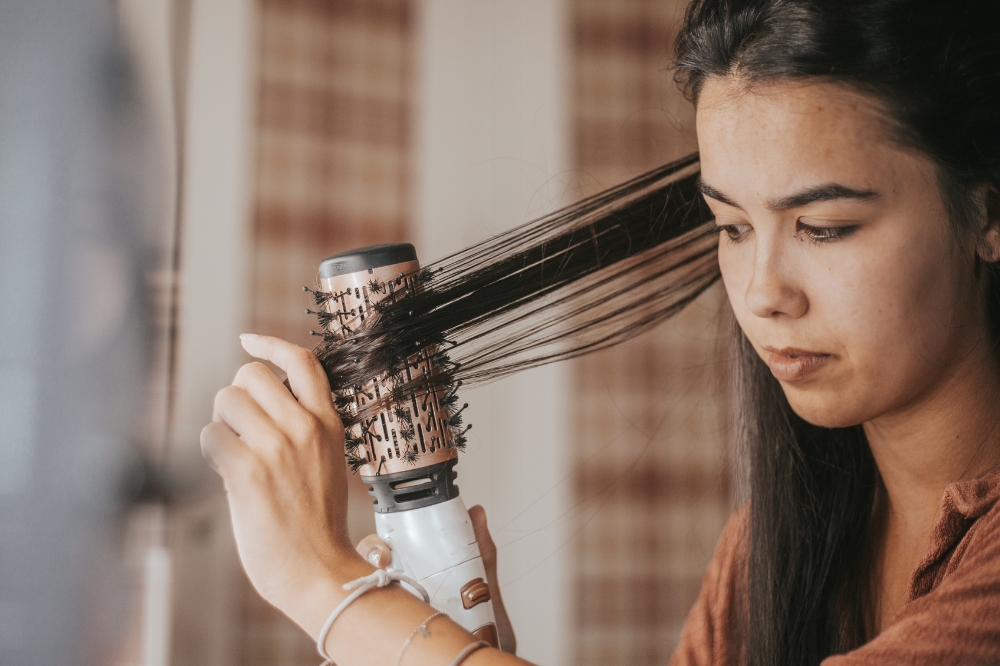 Menina secando o cabelo com escova secadora