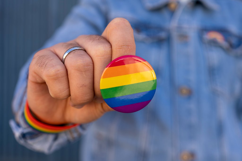 Homem irreconhecível mostrando para a câmera um broche LGBT de arco-íris. Orgulho de gays, lésbicas, bissexuais e trans, respeito pela diversidade de orientação sexual e identidade de gênero.