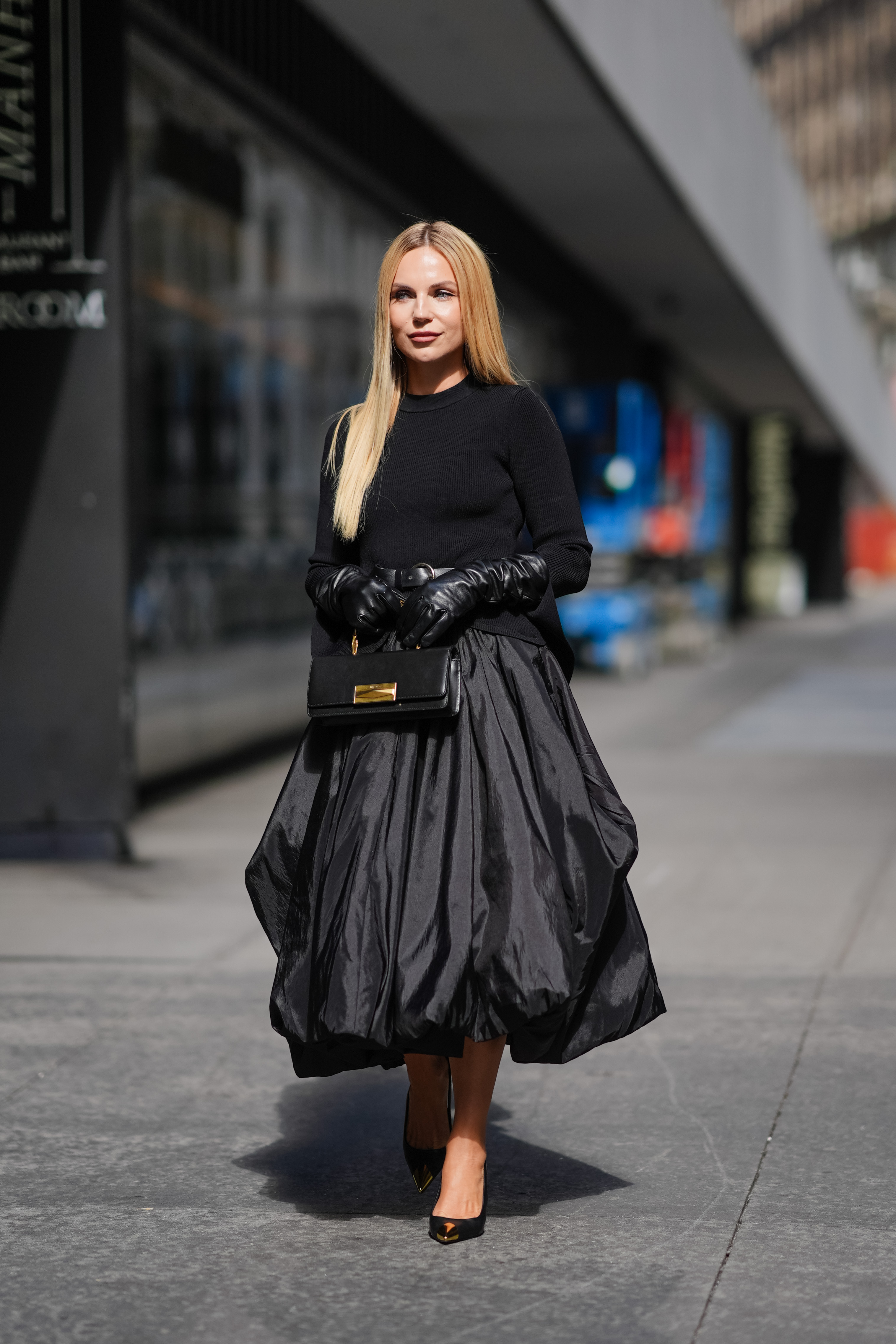 Mulher usando look todo preto com saia midi balonê, blusa de manga comprida, luvas e scarpin