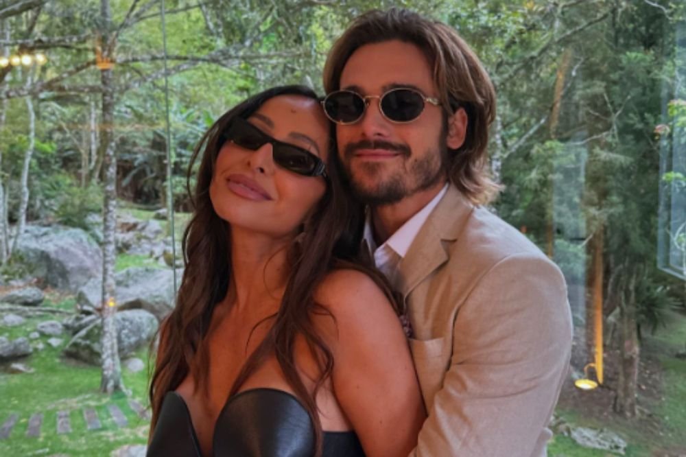 Sabrina Sato e Nicolas Prattes posando juntos; eles estão abraçados, sorrindo e usam óculos de sol