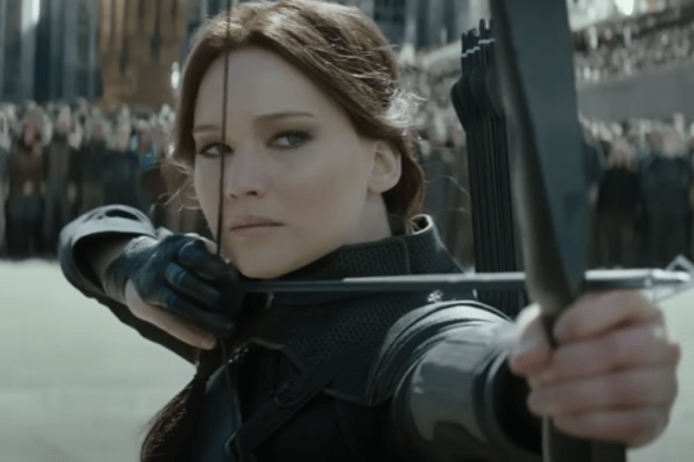 Cena de Katniss com arco e flecha em Jogos Vorazes: A Esperança - O Final; ela está com expressão séria enquanto mira para atirar