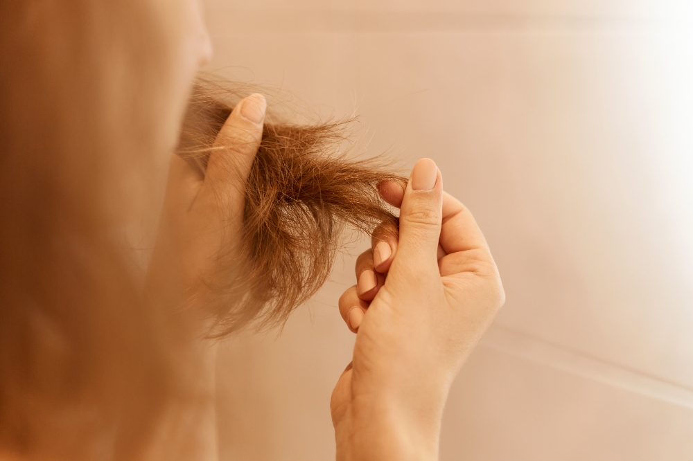 Mulher olhando para cabelo danificado no banheiro