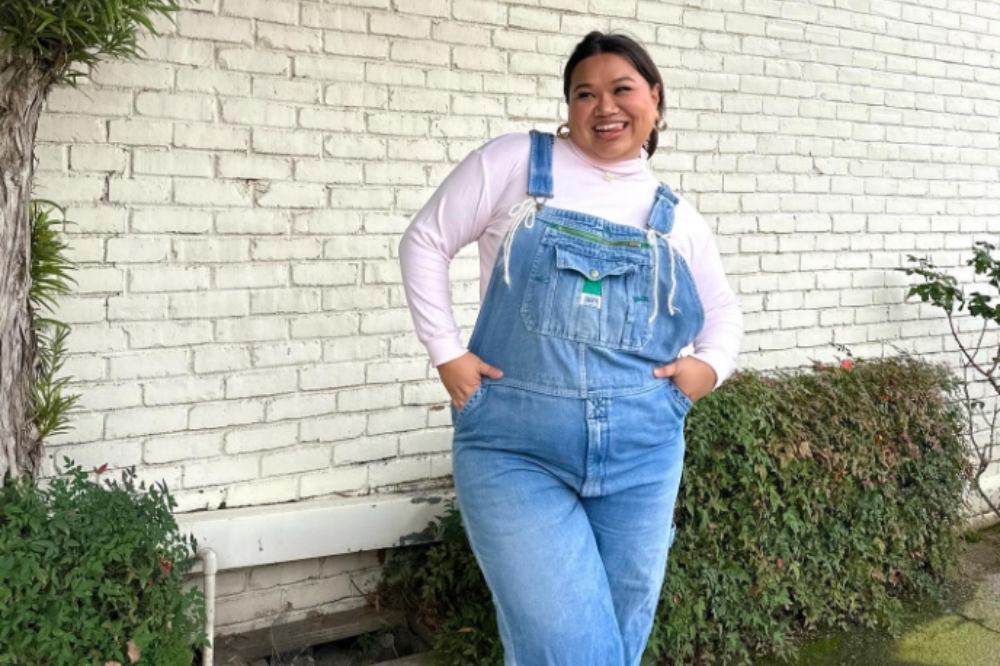 Garota usa blusa branca de gola alta e manga longa por baixo de macacão jeans