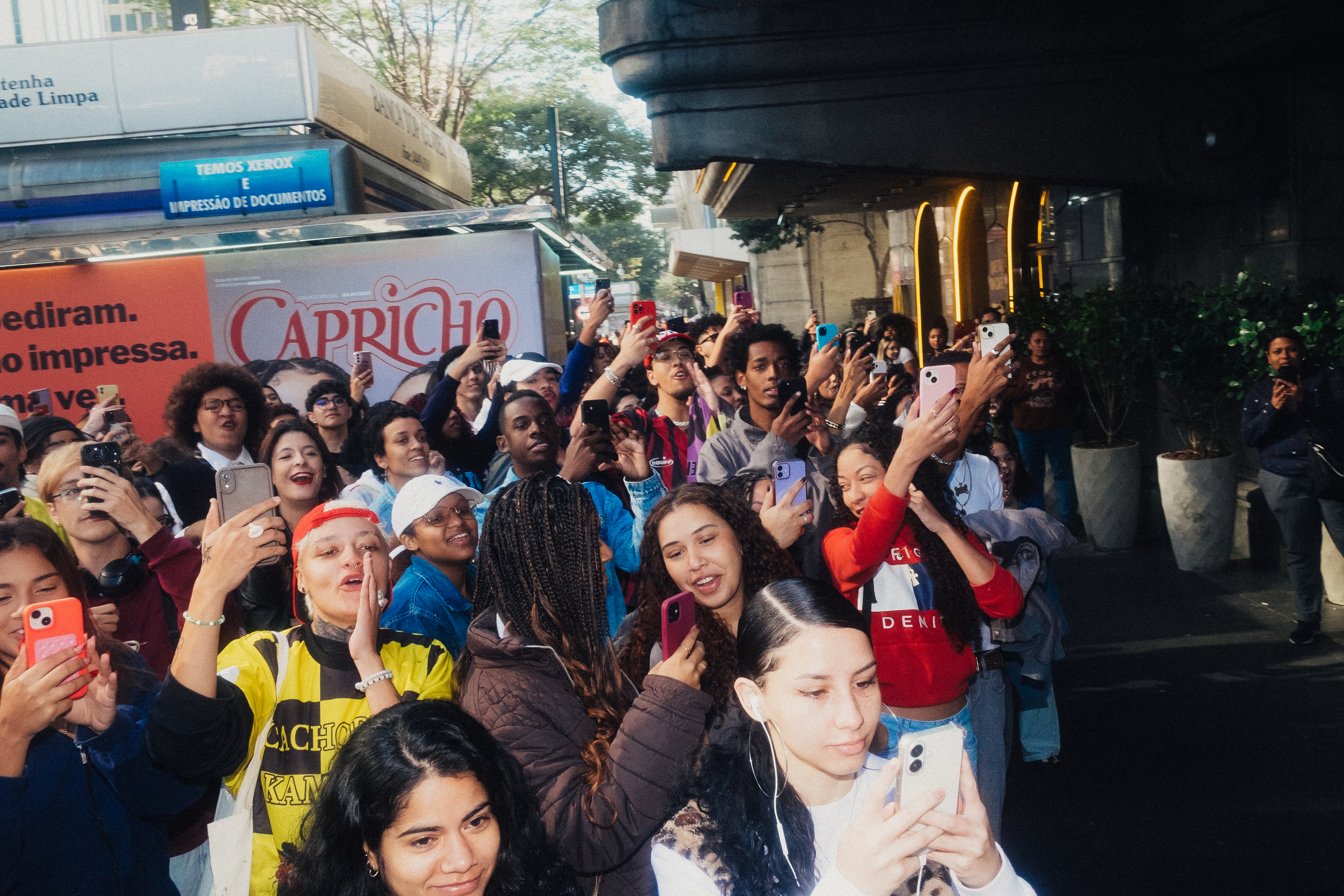 Tasha & Tracie com fãs na ação em banca 7 Multidão de fãs aguardam em frente a banca, eles estão com os celulares erguidos, enquanto gritam