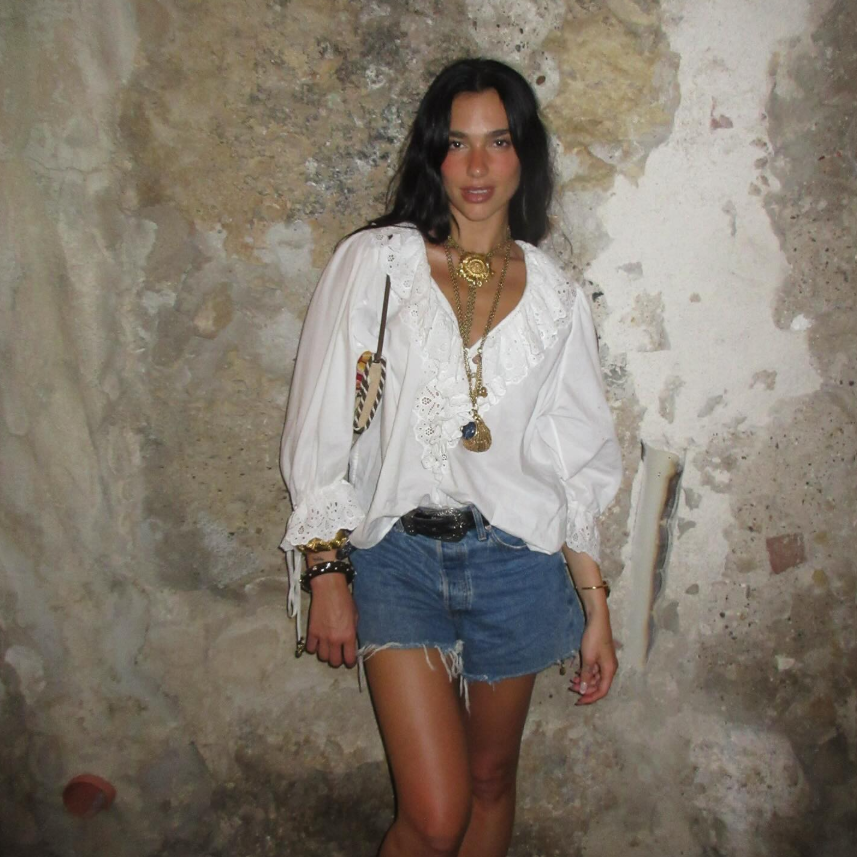 Dua Lipa usando look boho com short jeans e camisa branca