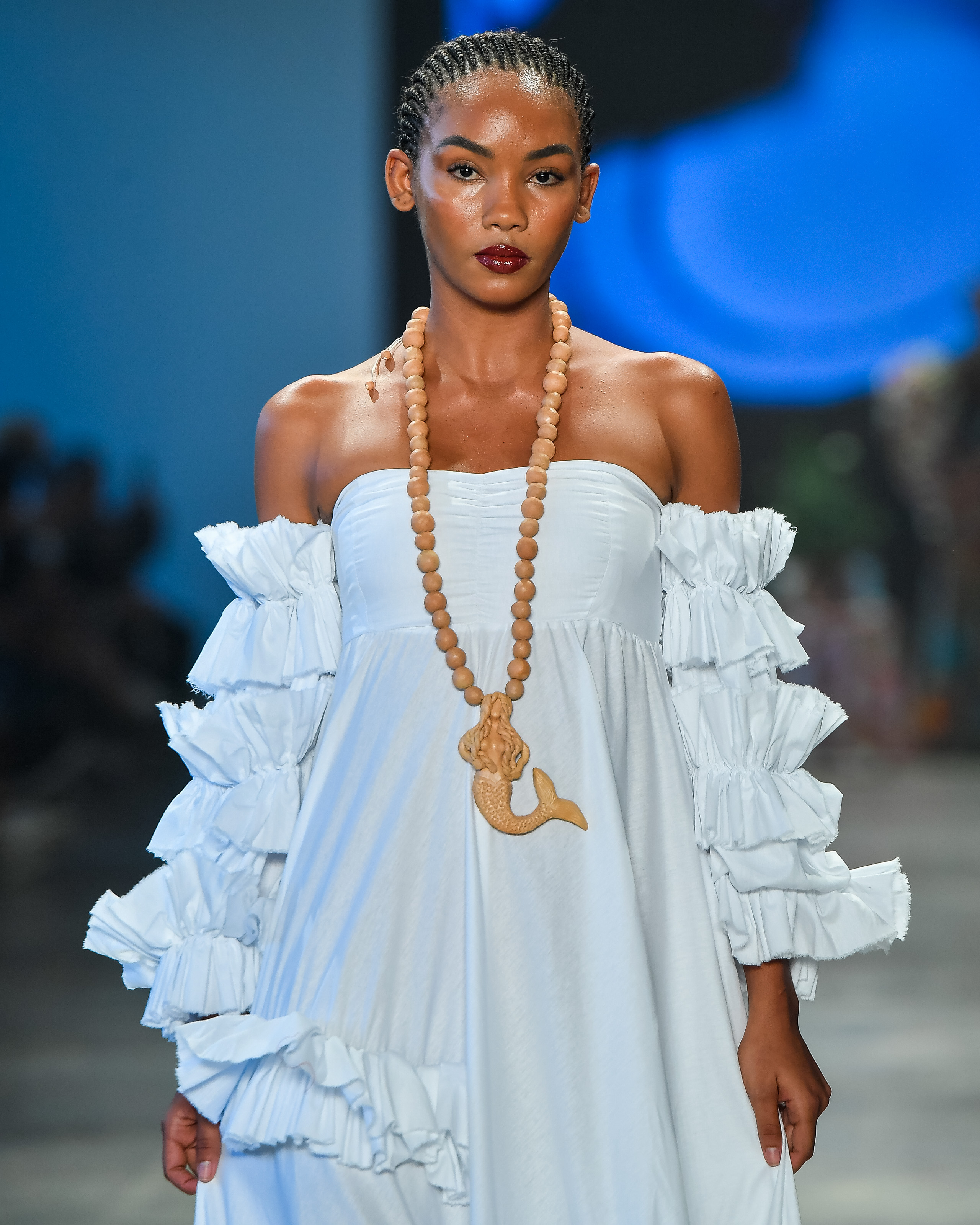 Modelo desfilando no desfile da marca Meninos Rei SPFW N60 com look laranja, pele iluminada e lábios avermelhados