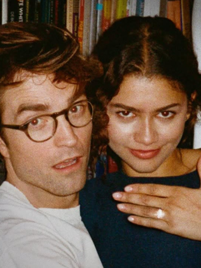 Zendaya e Robert Pattinson estão abraçados, ele usa roupa branca e ela roupa preta, enquanto exibe um anel de noivado