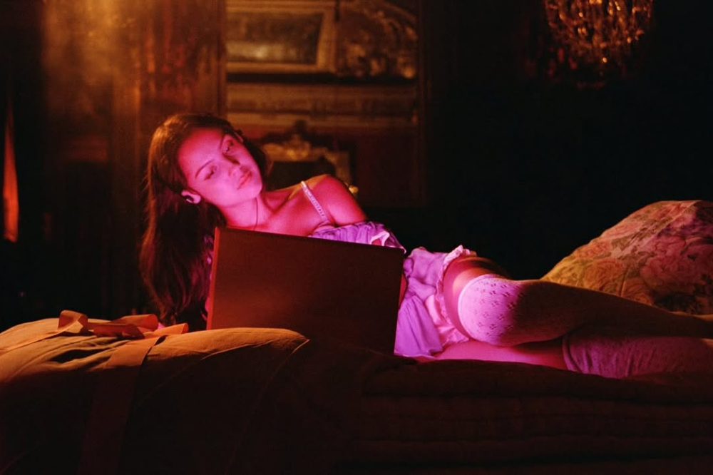 Mulher deitada na cama usando notebook, com iluminação quente e clima íntimo.