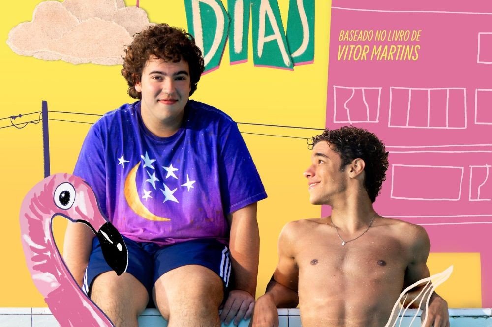 Dois jovens sorridentes em uma piscina. Um, de camiseta roxa com lua e estrelas, senta na borda com uma boia de flamingo rosa. O outro, sem camisa, está na água, olhando para o lado. O fundo é um desenho colorido de casas e nuvens, com o texto BASEADO NO LIVRO DE VITOR MARTINS