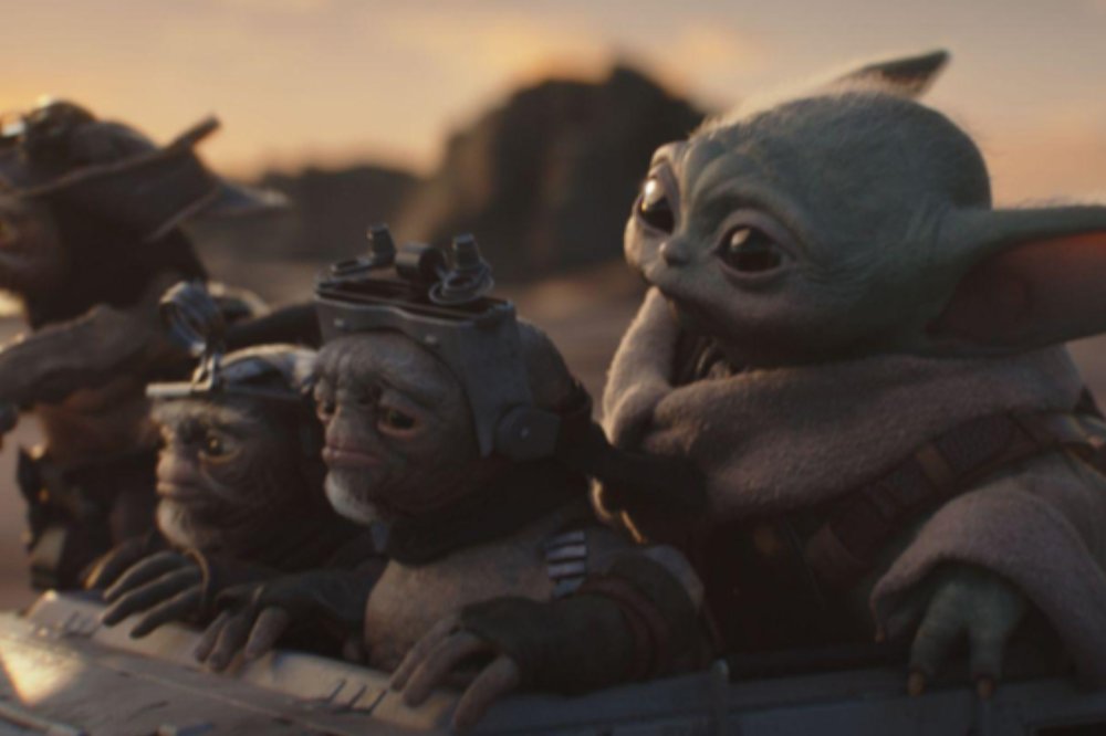 Grogu, o Baby Yoda, em um veículo com três alienígenas pequenos, um deles com barba branca e capacete, olhando para a frente, com um céu alaranjado ao fundo