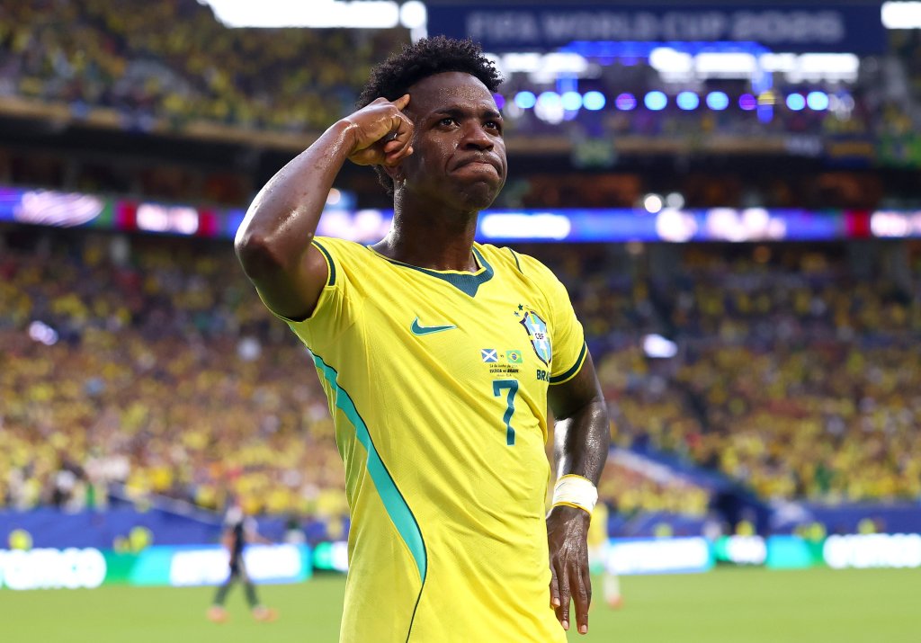 Jogador de futebol Vinicius Jr. comemora um gol, vestindo a camisa amarela da seleção brasileira com o número 7, em um estádio lotado