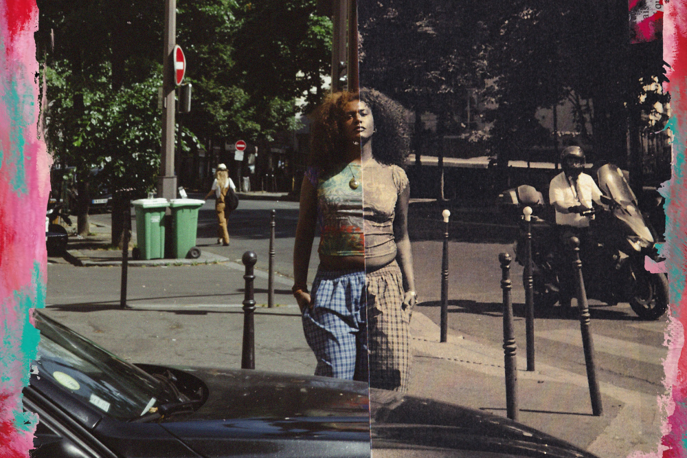 Mulher negra de cabelo crespo, blusa estampada e calça xadrez, dividida ao meio entre cores vibrantes e tons sépia, em rua movimentada com carros, lixeiras e pessoas ao fundo