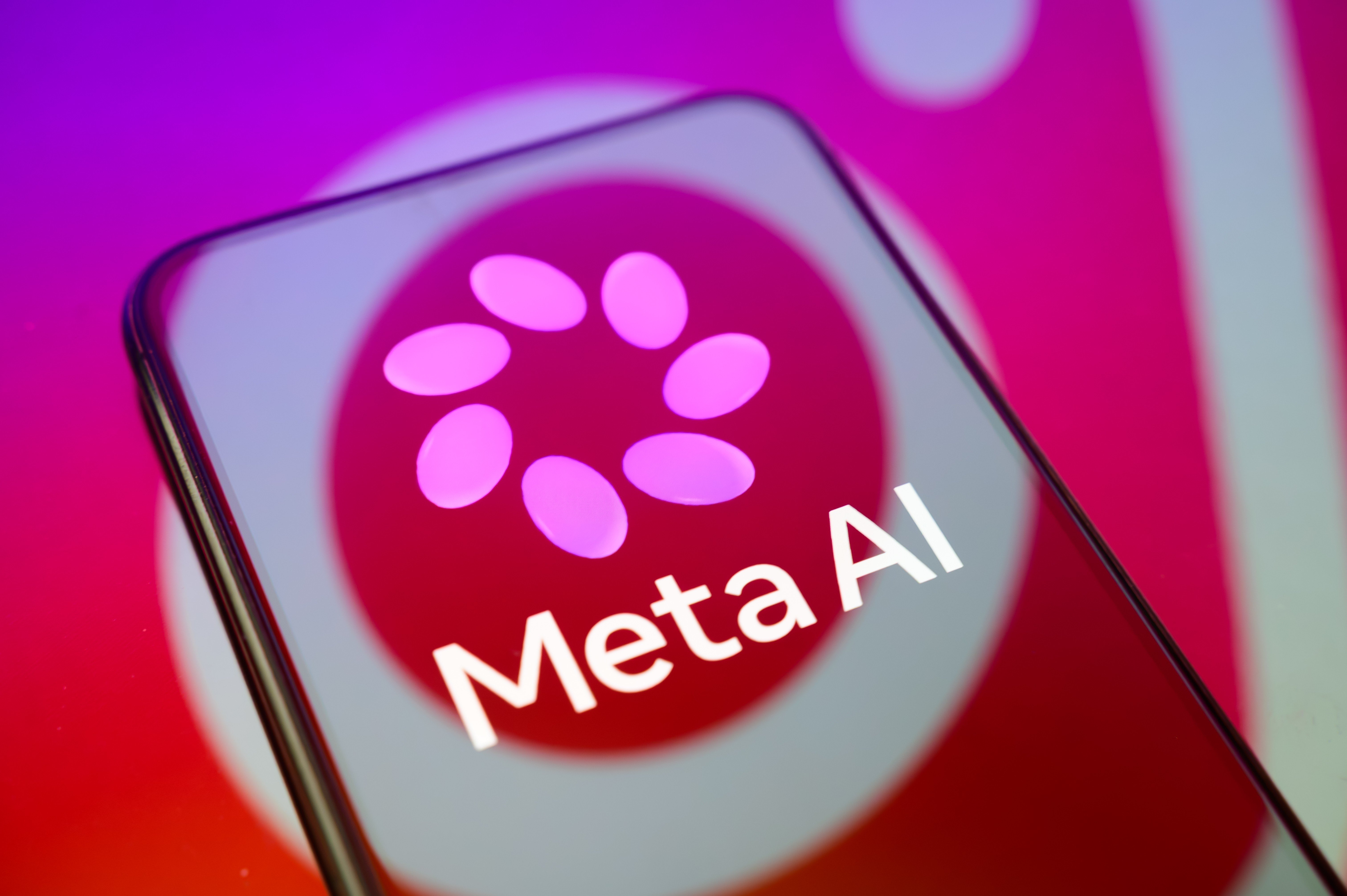 Smartphone preto exibindo o logo Meta AI em tela vermelha com seis ovais rosa formando um círculo, sobre fundo roxo e rosa
