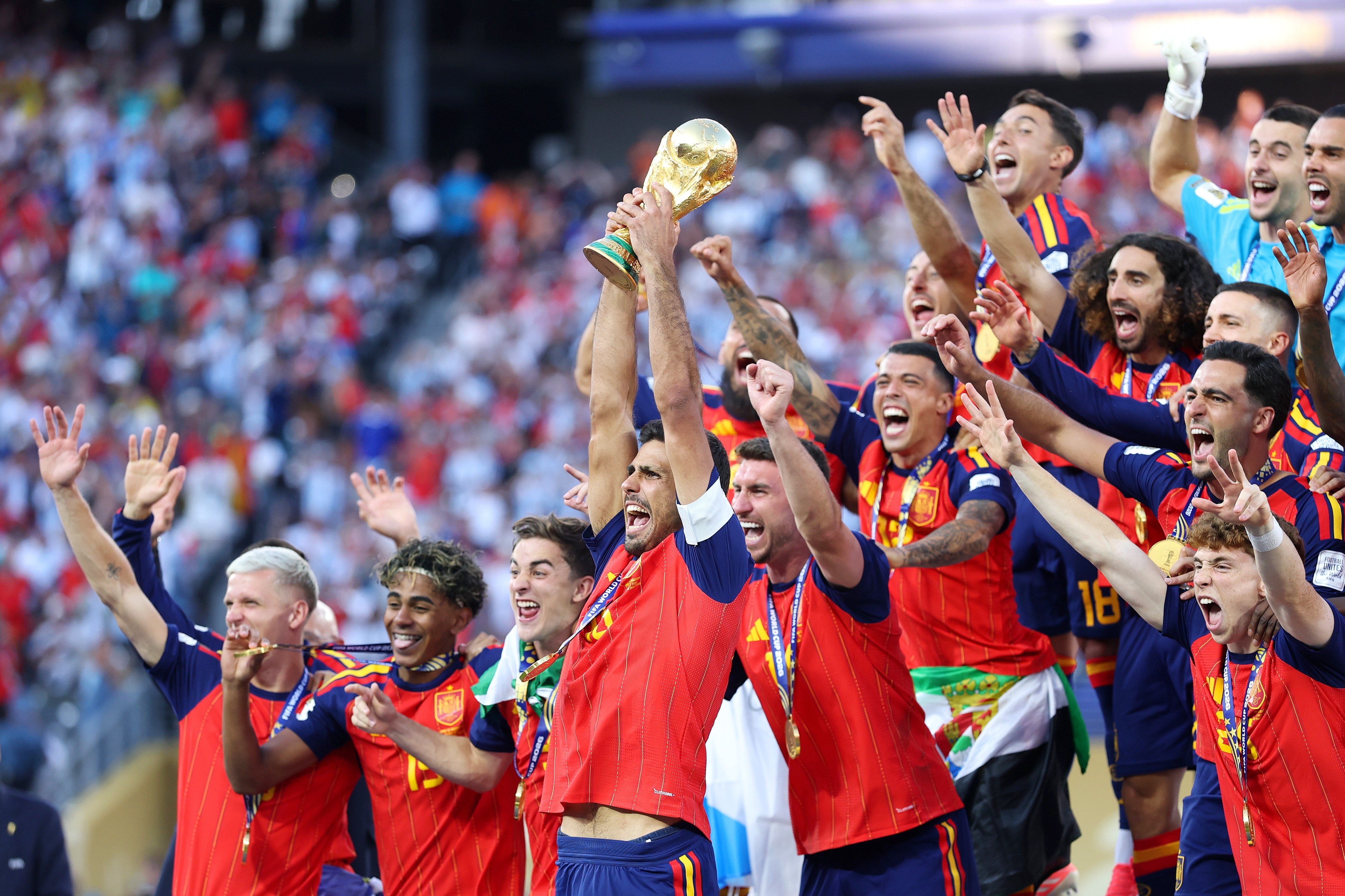 Jogadores da seleção espanhola de futebol, vestindo uniformes vermelhos e azuis, celebram a vitória erguendo a taça dourada do campeonato. Eles sorriem e gritam de alegria, com medalhas de ouro no pescoço, em um estádio lotado