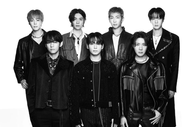 Sete homens jovens, membros do grupo BTS, posam em preto e branco. Eles vestem jaquetas e casacos escuros com detalhes em couro, correntes e franjas, exibindo expressões sérias e confiantes.