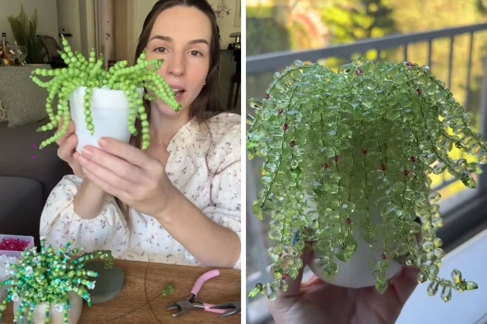 Mulher sorridente segura um vaso branco com uma planta pendente feita de miçangas verdes, enquanto outra planta similar e ferramentas de artesanato estão sobre uma mesa de madeira. À direita, uma mão segura um vaso branco com uma planta pendente de miçangas verdes translúcidas, com pequenos pontos vermelhos, contra um fundo desfocado de varanda e vegetação