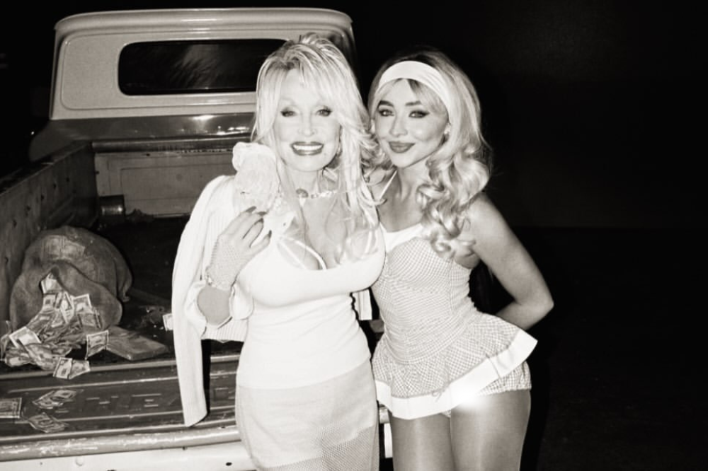 Dolly Parton e Sabrina Carpenter sorrindo, abraçadas, em preto e branco. Dolly usa blusa justa e casaco nos ombros. Sabrina veste top e shorts com babados, faixa na cabeça. Ao fundo, caçamba de caminhonete com notas de dólar espalhadas